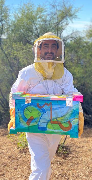 Steve in bee suit holding a colorful painted bee box at the sanctuary